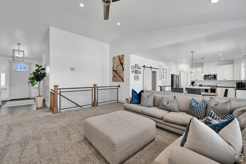 Carpeted living area with a chandelier, vaulted ceiling, a barn door, recessed lighting, and ceiling fan