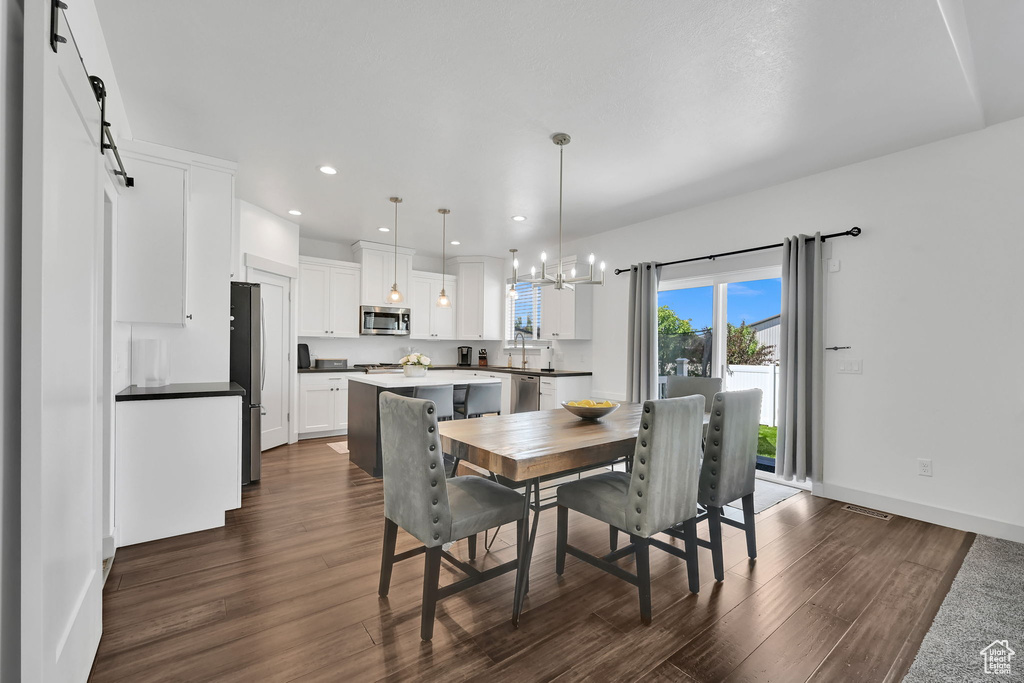 Dining space with a chandelier, dark wood-type flooring, recessed lighting, baseboards, and a barn door