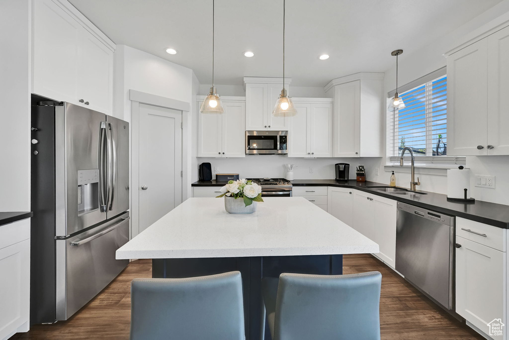 Kitchen with stainless steel appliances, a sink, a center island, white cabinets, and dark wood-style floors