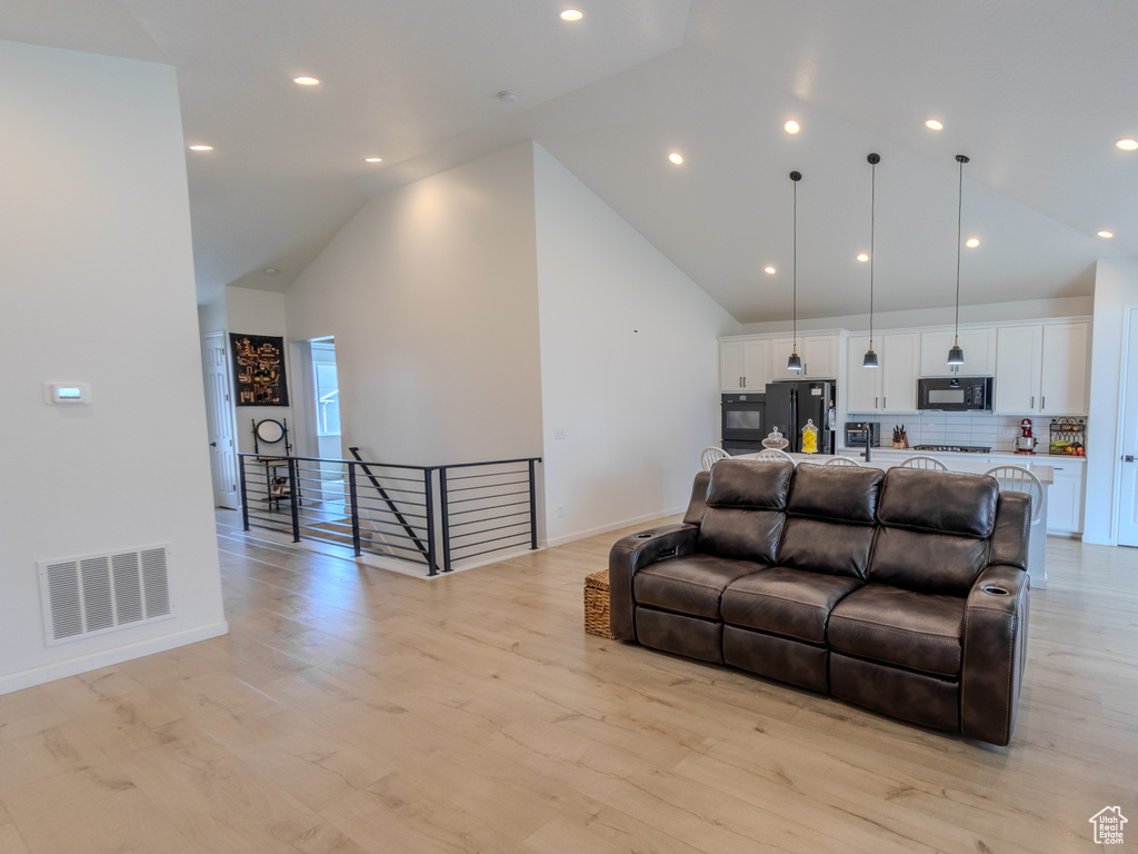 Living room with high vaulted ceiling, baseboards, light wood finished floors, and recessed lighting