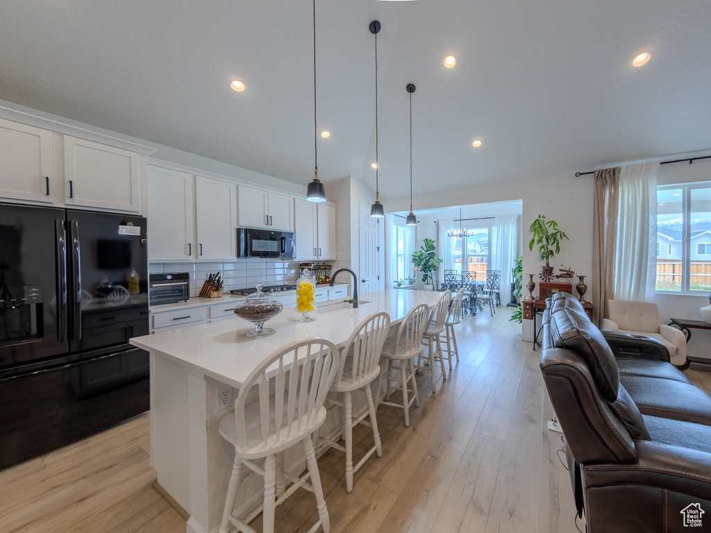 Kitchen featuring black appliances, light countertops, backsplash, a kitchen breakfast bar, and recessed lighting