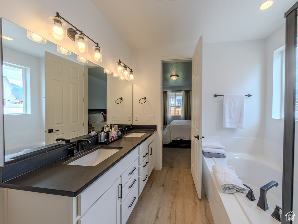 Ensuite bathroom featuring wood finished floors, double vanity, and a garden tub