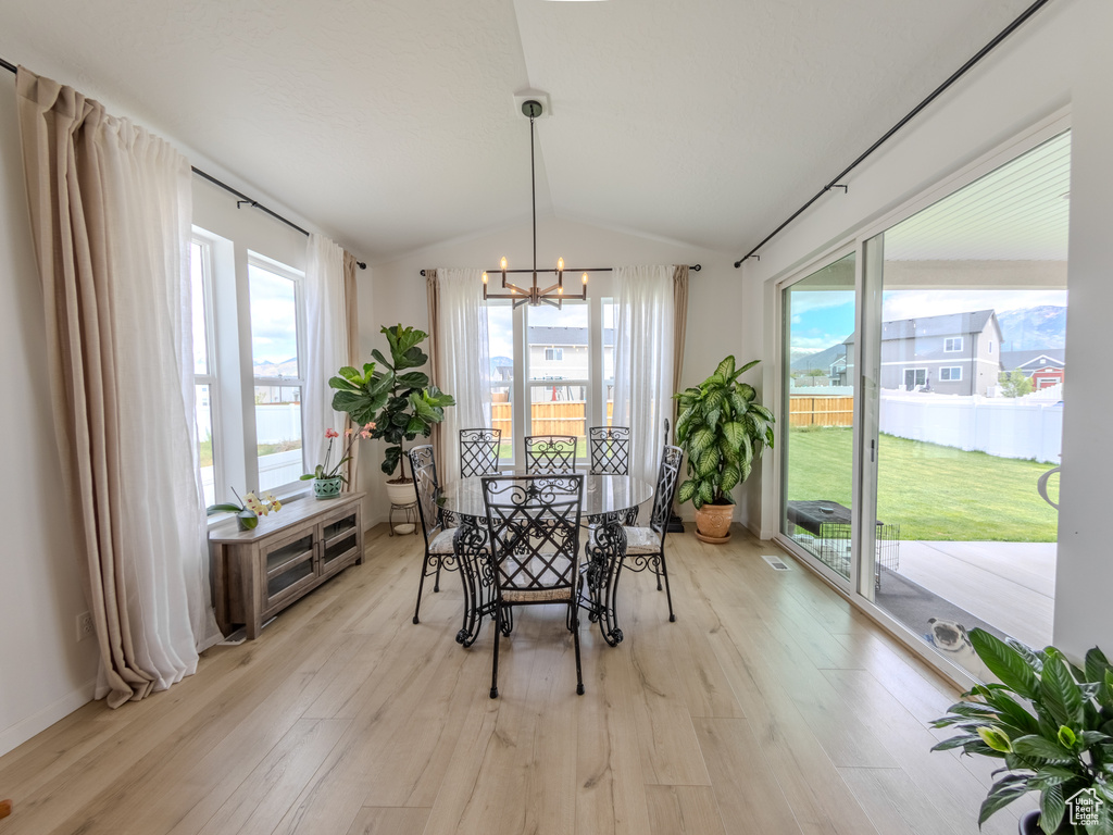 Dining room featuring light wood-type flooring, lofted ceiling, a chandelier, and plenty of natural light