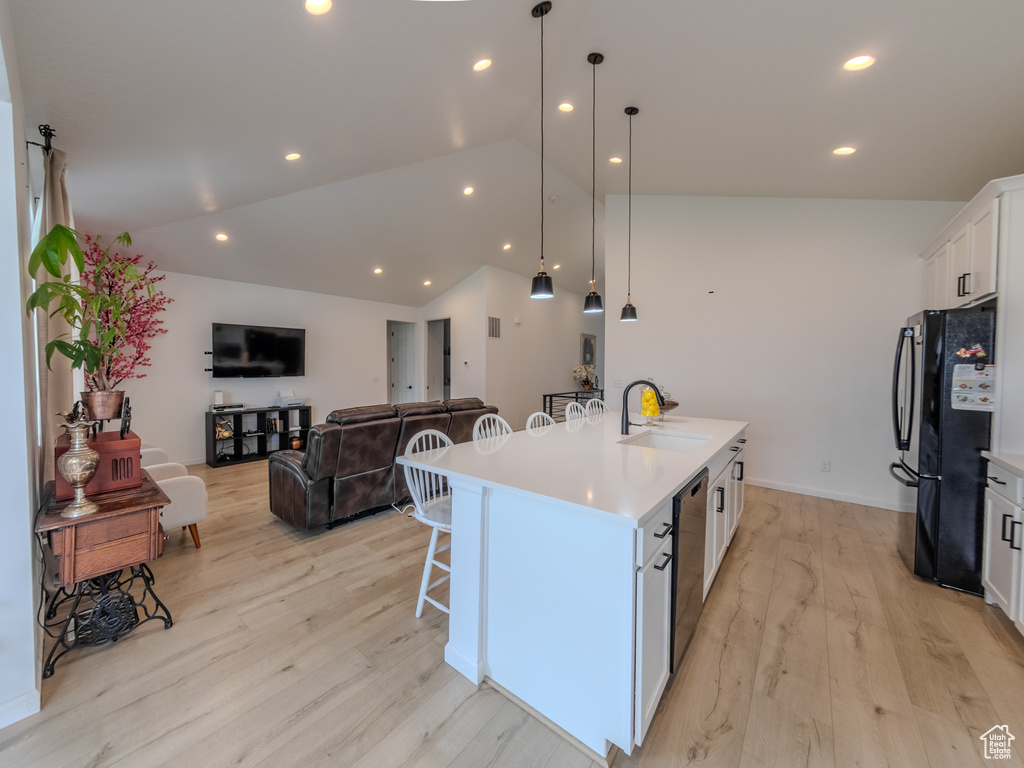 Kitchen featuring a sink, black appliances, a center island with sink, light wood-style floors, and white cabinets