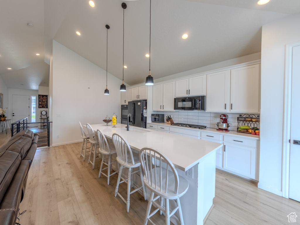 Kitchen featuring black appliances, a large island, a kitchen breakfast bar, backsplash, and light wood-style flooring