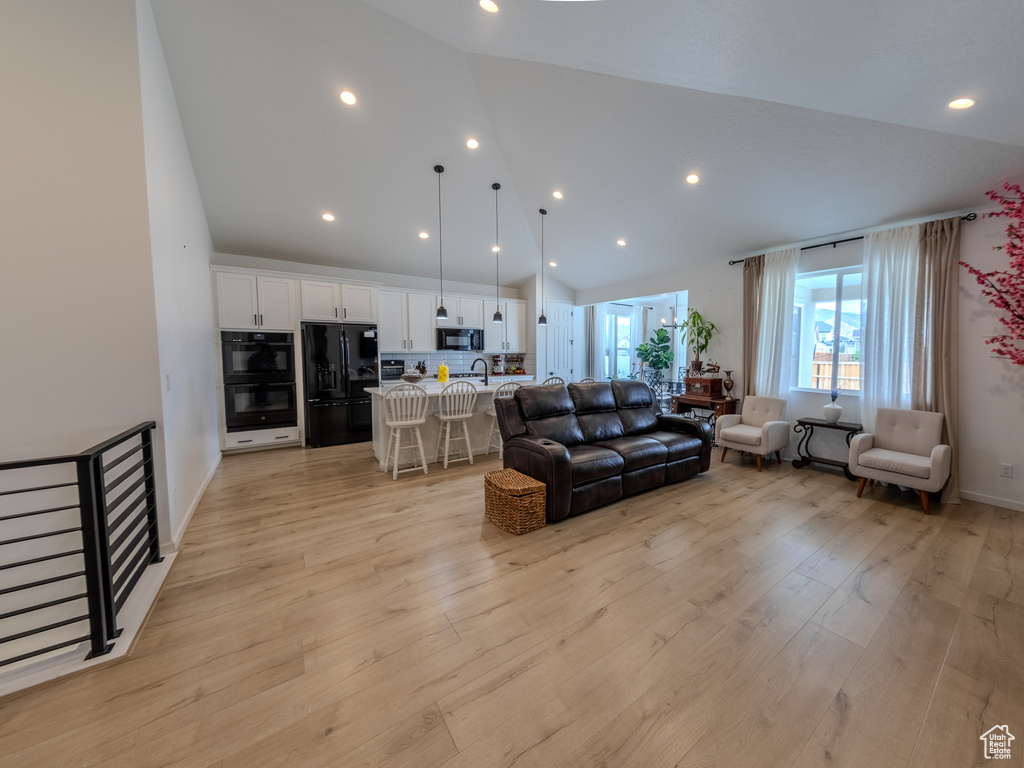 Living area with high vaulted ceiling, light wood-style flooring, and recessed lighting