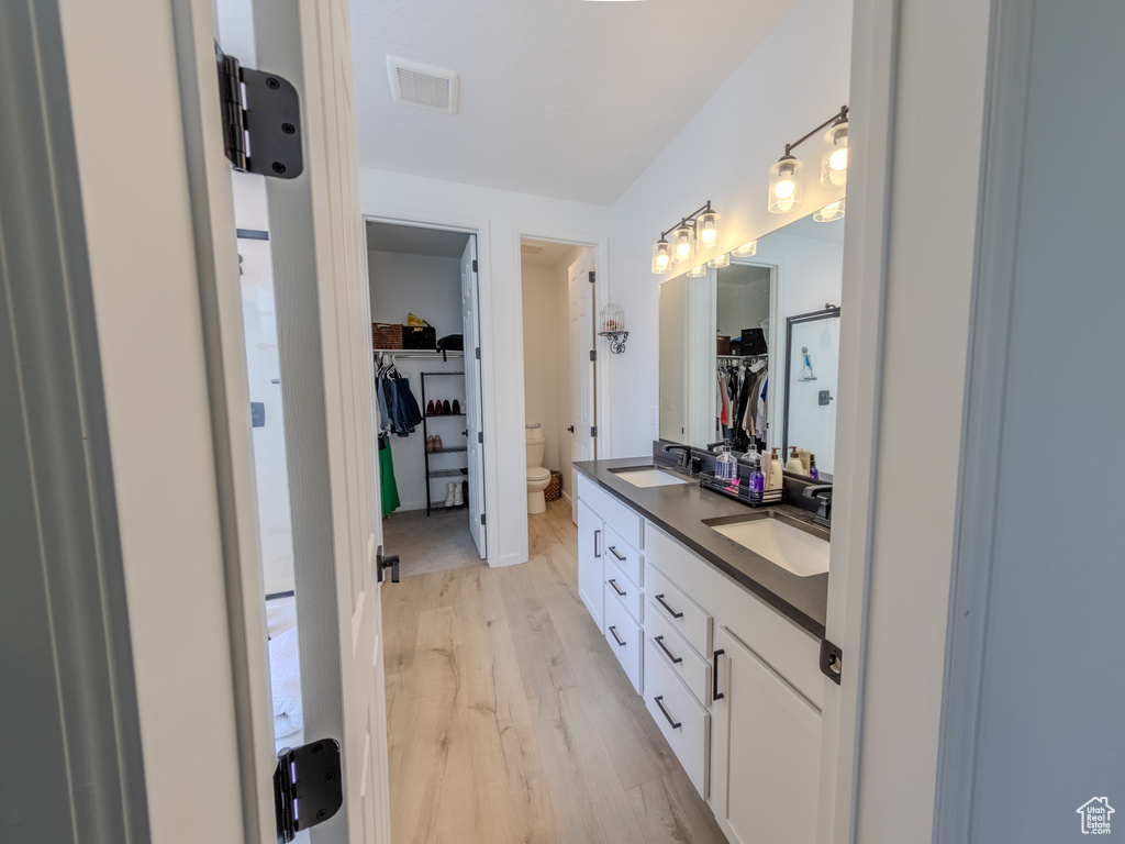 Full bathroom featuring toilet, wood finished floors, double vanity, and a spacious closet