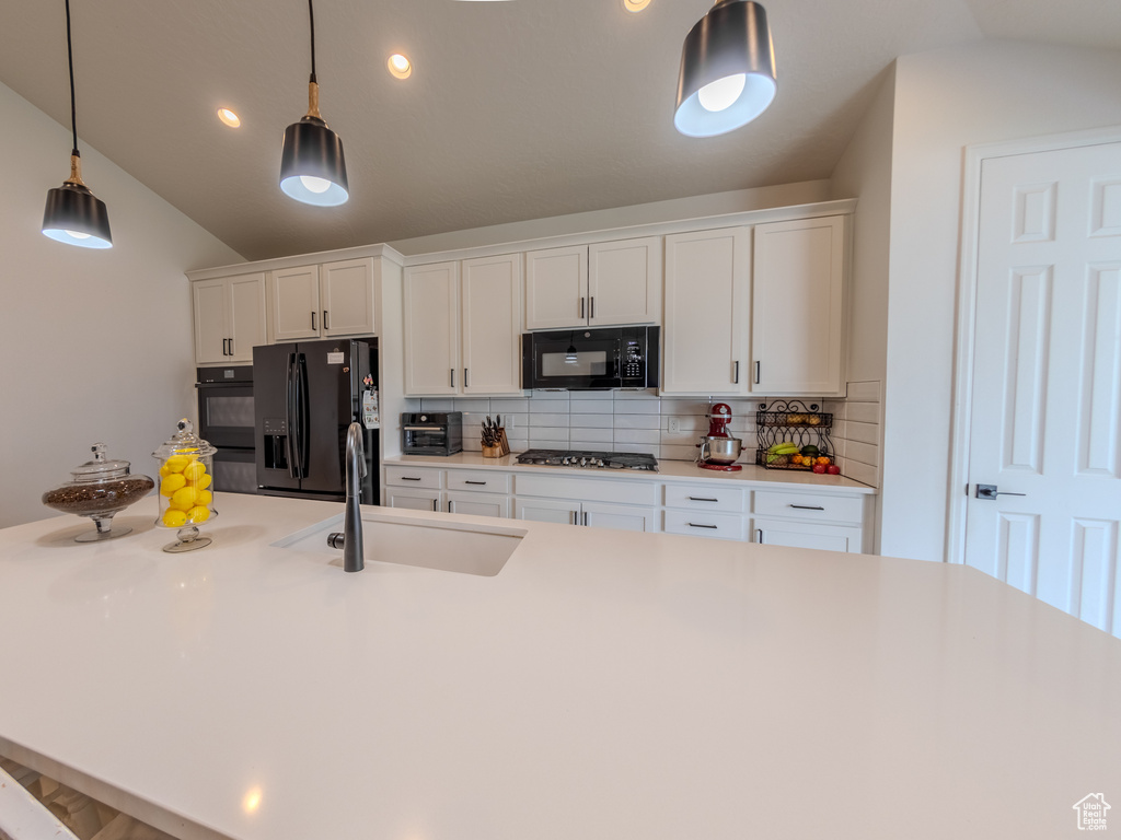 Kitchen with black appliances, a sink, vaulted ceiling, decorative backsplash, and white cabinetry