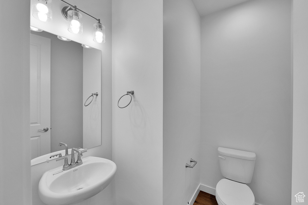 Half bathroom featuring a sink, toilet, wood finished floors, and baseboards