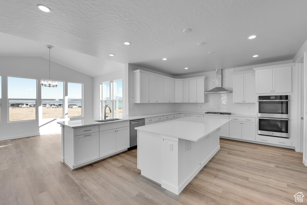 Kitchen featuring wall chimney exhaust hood, appliances with stainless steel finishes, a sink, a chandelier, and light countertops