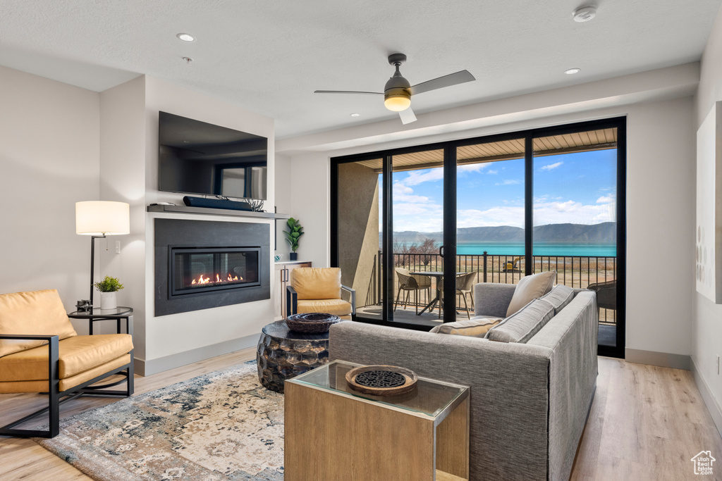 Living room with a glass covered fireplace, wood finished floors, ceiling fan, baseboards, and recessed lighting