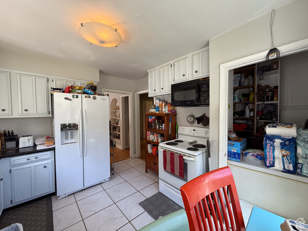 Kitchen featuring white appliances, light tile patterned flooring, and white cabinets