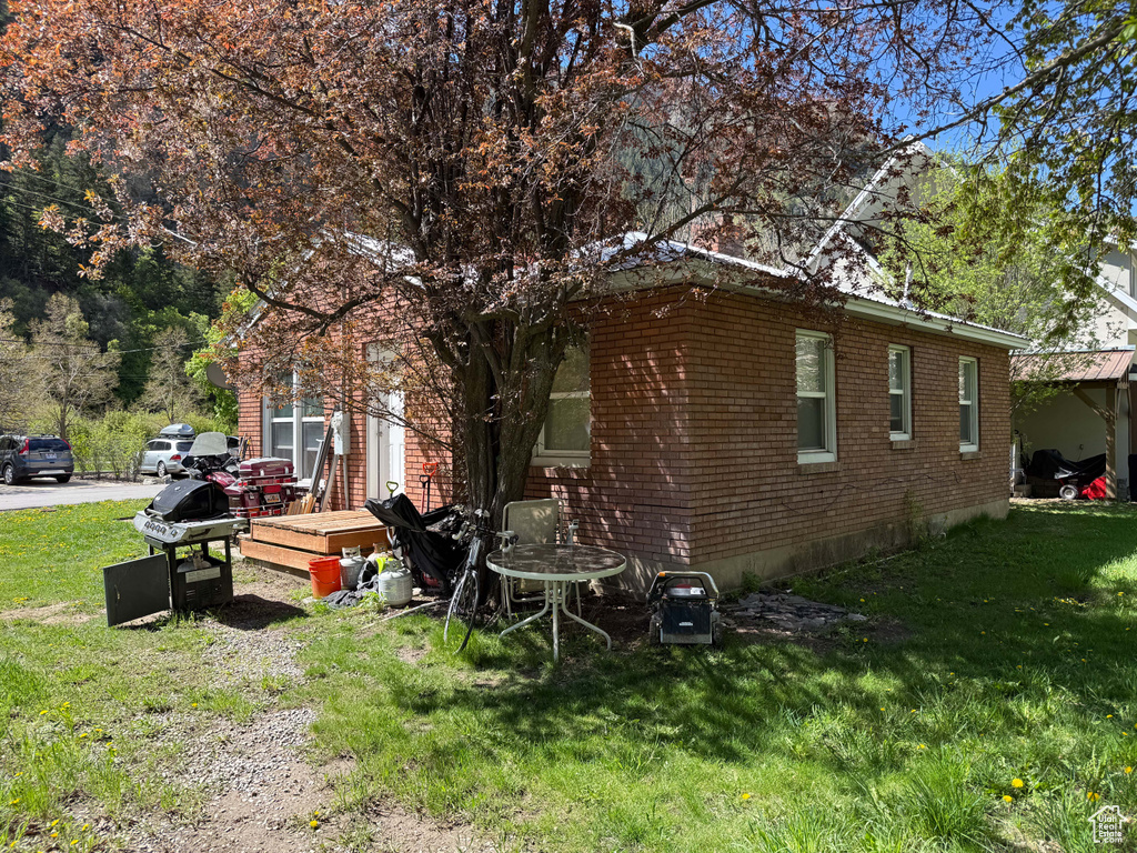 View of side of property with a deck, a lawn, and brick siding