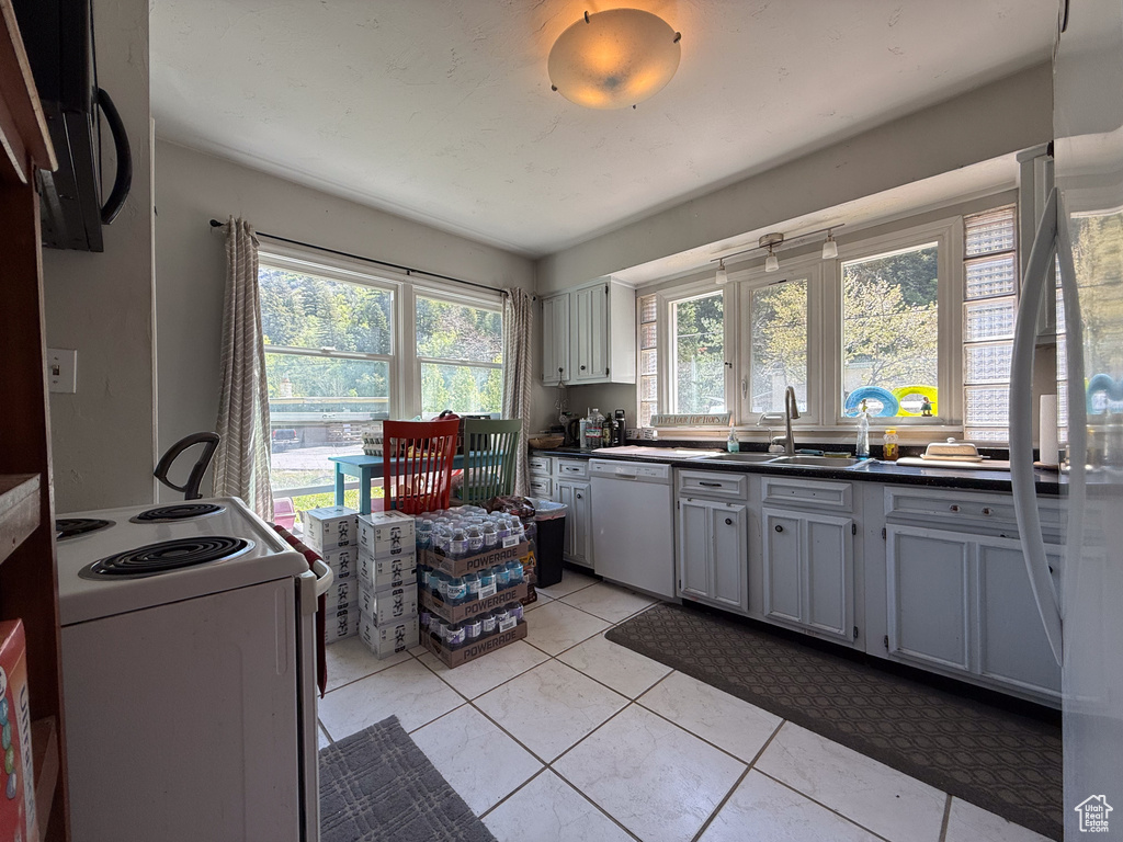 Kitchen featuring white appliances, a sink, dark countertops, and light tile patterned floors