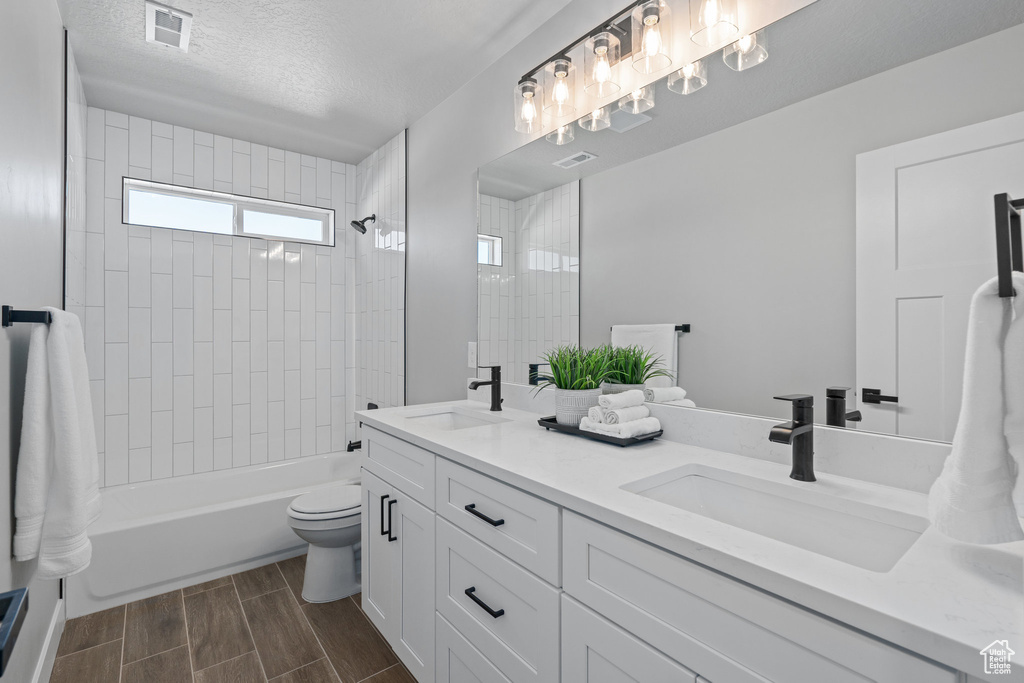Bathroom with toilet, wood tiled floors,  shower combination, double vanity, and a textured ceiling