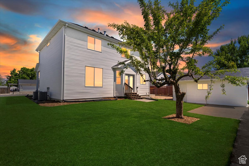 View of front of property with entry steps, a lawn, and central AC