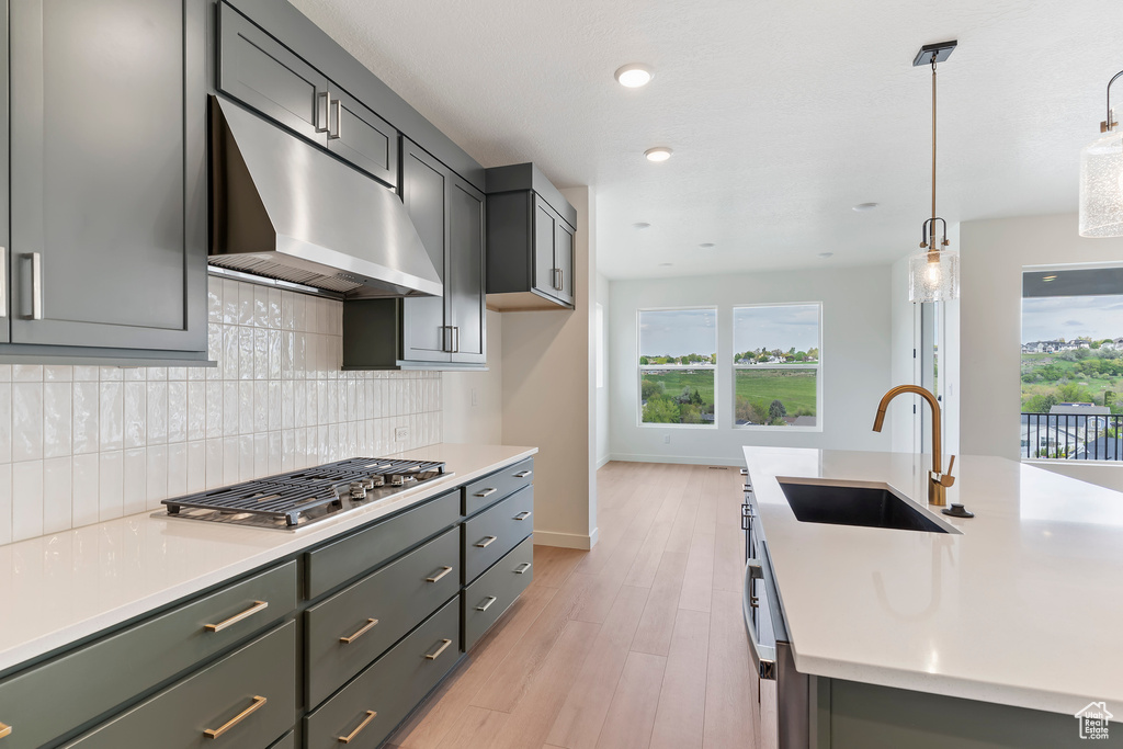 Kitchen featuring a sink, under cabinet range hood, stainless steel gas cooktop, light countertops, and recessed lighting