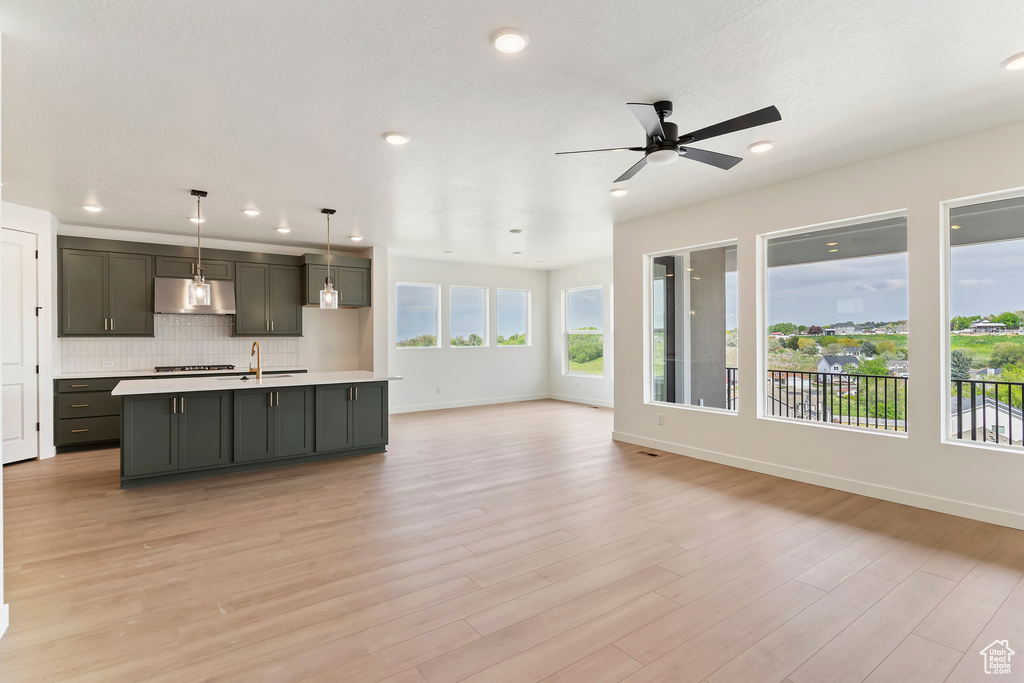 Kitchen with a ceiling fan, under cabinet range hood, light countertops, recessed lighting, and open floor plan