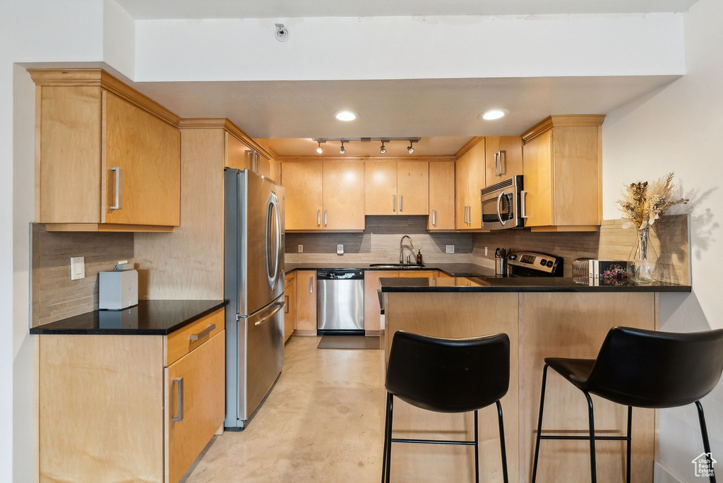 Kitchen featuring stainless steel appliances, a peninsula, track lighting, finished concrete floors, and light brown cabinetry