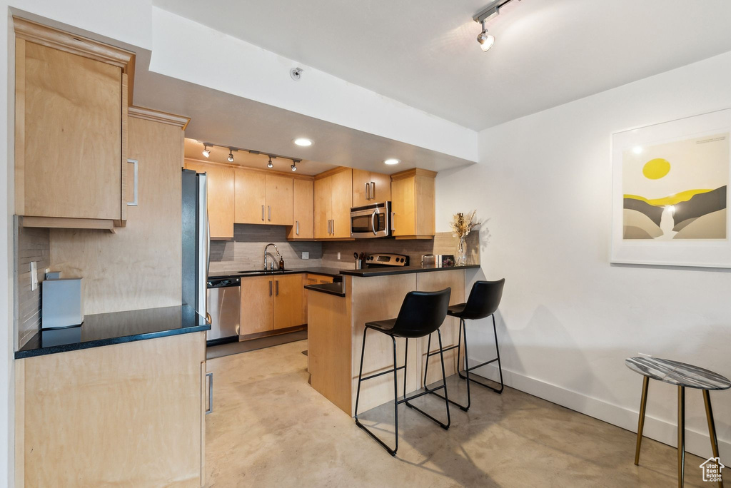 Kitchen featuring track lighting, stainless steel appliances, light brown cabinetry, baseboards, and a peninsula