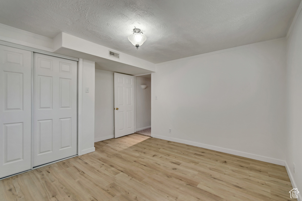 Unfurnished bedroom with light wood-type flooring, baseboards, a textured ceiling, a closet, and crown molding
