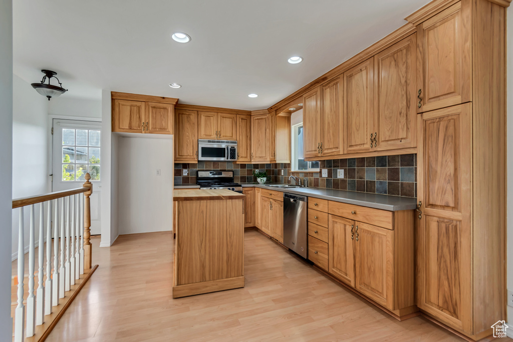 Kitchen featuring appliances with stainless steel finishes, a center island, tasteful backsplash, light wood-style flooring, and recessed lighting