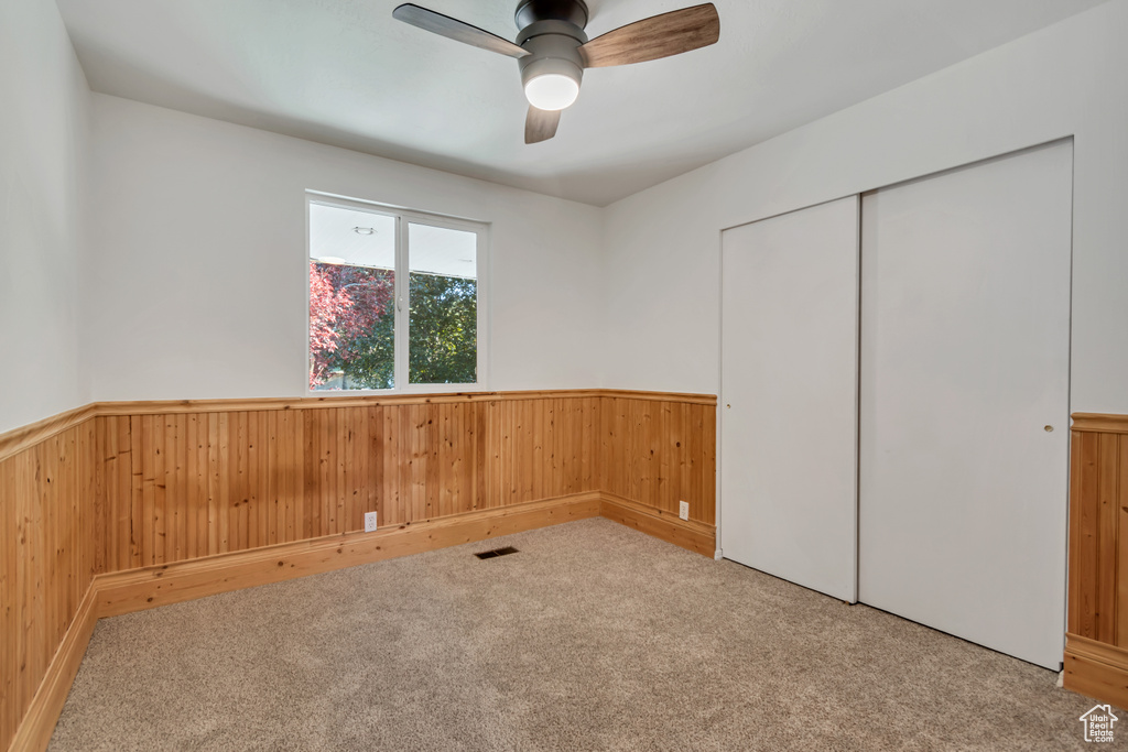 Unfurnished bedroom featuring wood walls, a wainscoted wall, carpet, a closet, and ceiling fan