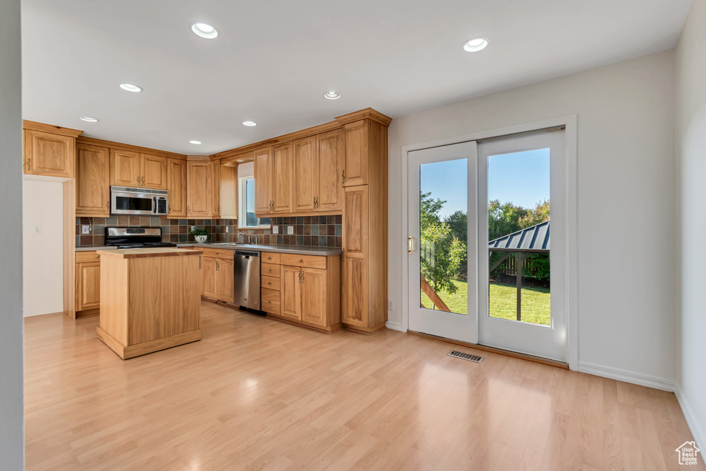 Kitchen with stainless steel appliances, backsplash, a center island, light wood finished floors, and recessed lighting