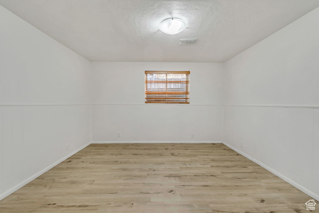 Unfurnished room featuring light wood-style floors, baseboards, and a textured ceiling