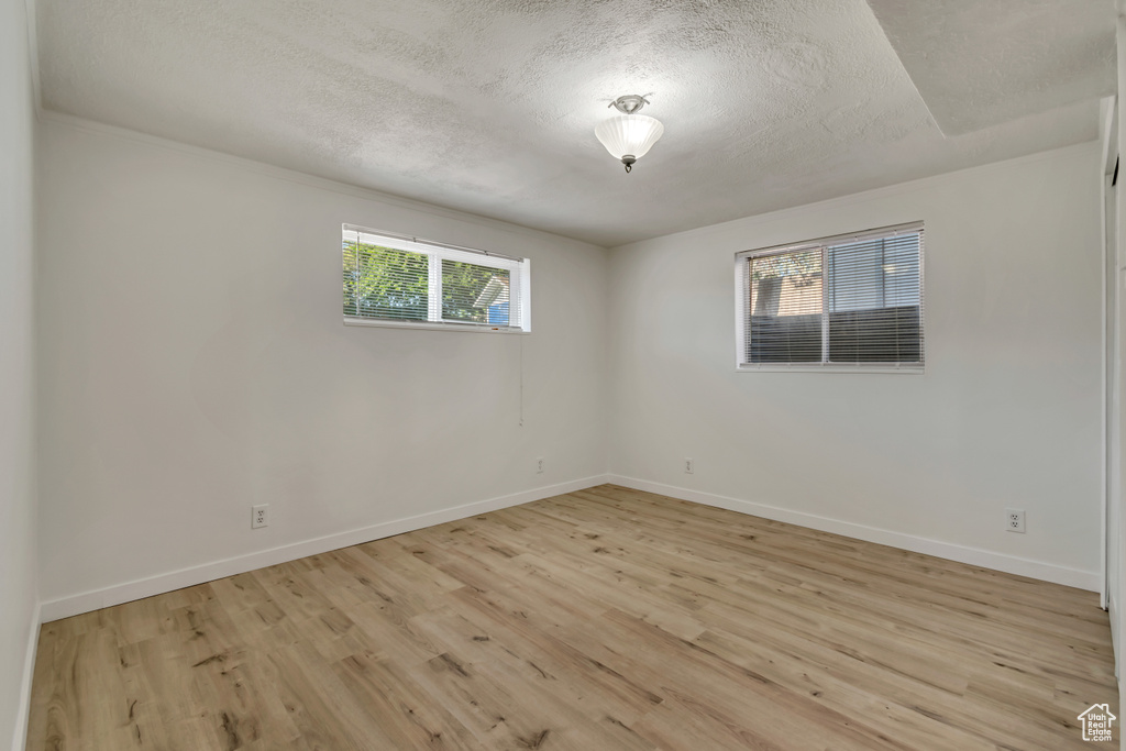 Empty room with healthy amount of natural light, a textured ceiling, light wood-type flooring, and baseboards