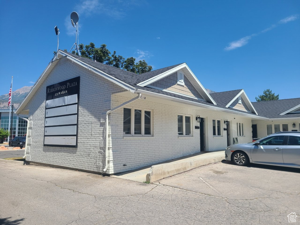 View of front of property featuring brick siding and roof with shingles