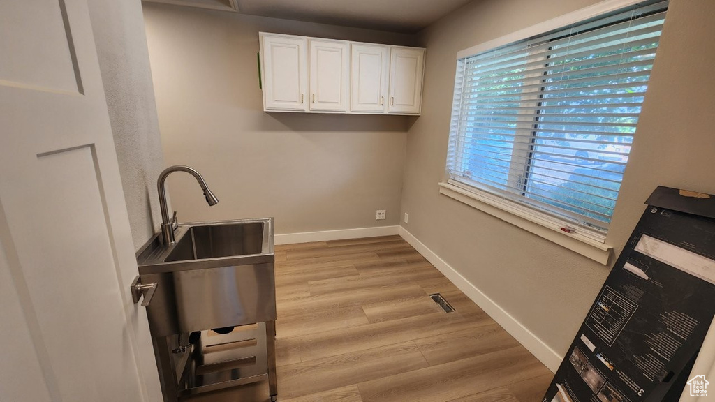 Laundry area with light wood-type flooring, baseboards, and a sink
