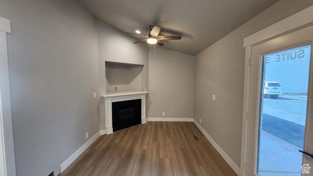 Unfurnished living room with a ceiling fan, vaulted ceiling, a glass covered fireplace, wood finished floors, and baseboards