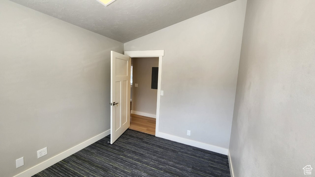 Empty room with lofted ceiling, baseboards, and dark carpet