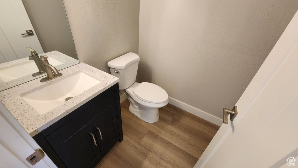 Half bathroom with toilet, vanity, wood finished floors, and baseboards