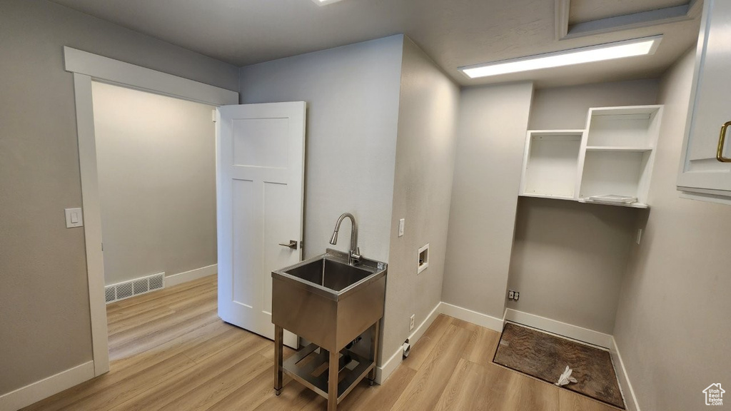 Laundry room featuring light wood-type flooring, a sink, and baseboards