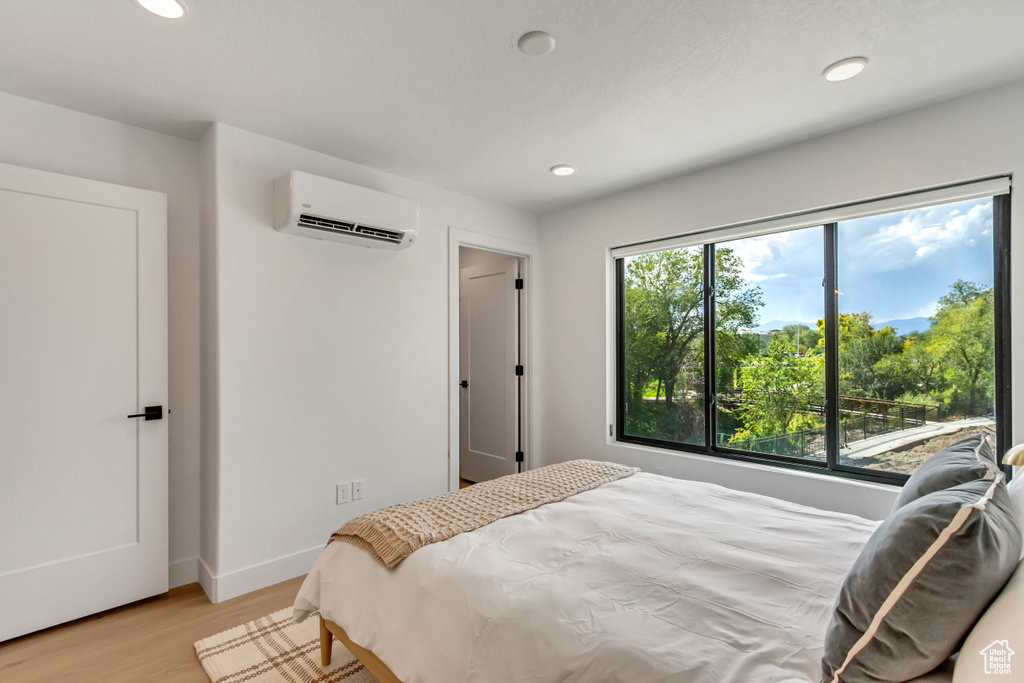 Bedroom with a wall mounted AC, recessed lighting, light wood-type flooring, and baseboards