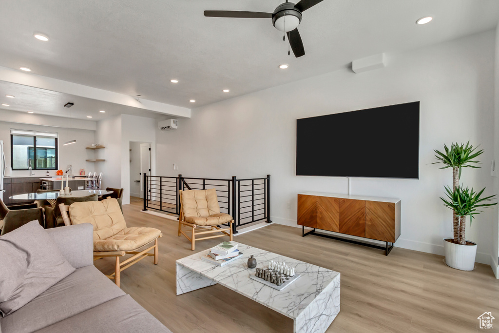 Living area featuring light wood-type flooring, ceiling fan, recessed lighting, a wall mounted air conditioner, and baseboards