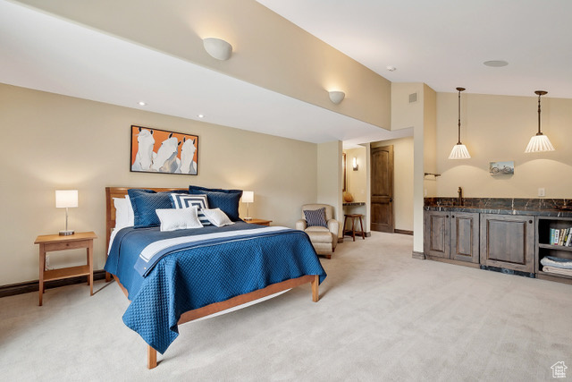 Bedroom with light colored carpet, bar with sink, lofted ceiling, and baseboards
