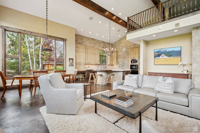 Living area with high vaulted ceiling, beamed ceiling, a chandelier, plenty of natural light, and finished concrete floors