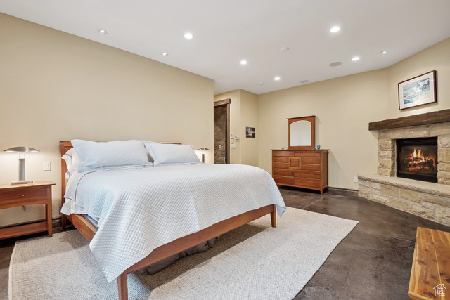 Bedroom featuring concrete flooring, recessed lighting, and a stone fireplace