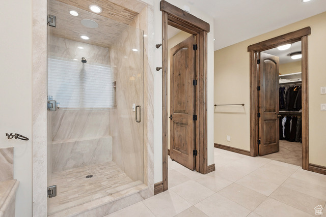 Bathroom with a marble finish shower, tile patterned flooring, baseboards, recessed lighting, and a walk in closet