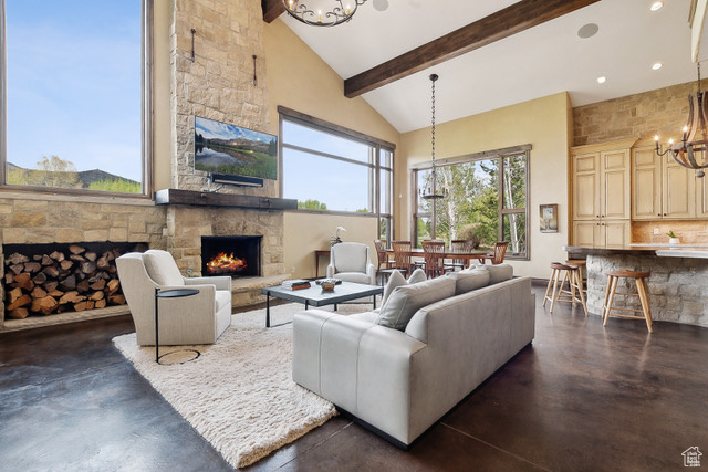 Living room featuring a chandelier, a fireplace, high vaulted ceiling, beam ceiling, and concrete floors
