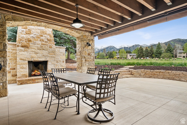 View of patio / terrace featuring an outdoor stone fireplace, a mountain view, a ceiling fan, and outdoor dining area