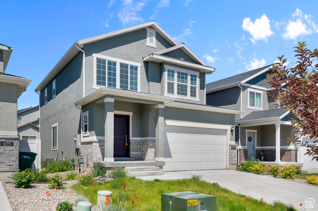 View of front of house with an attached garage, stucco siding, driveway, and stone siding