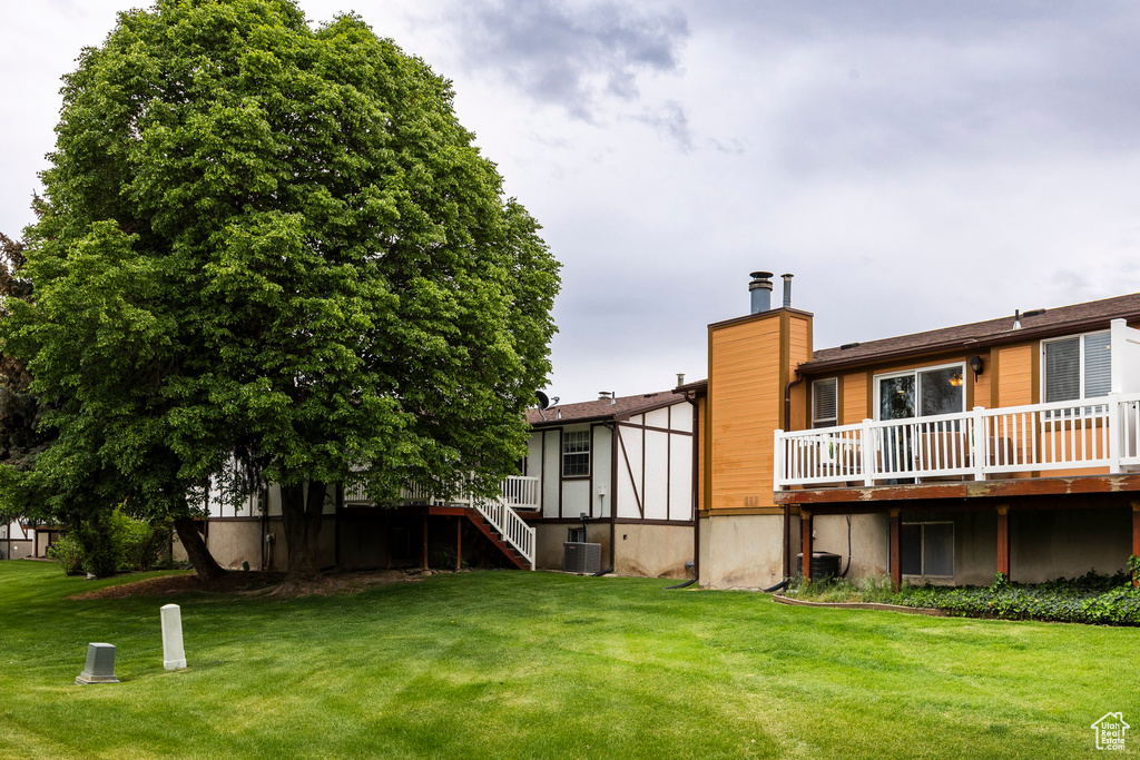 View of green lawn featuring central AC unit, a deck, and stairway