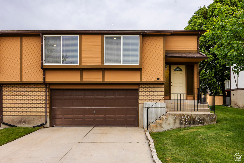 View of front of property with brick siding, a garage, driveway, and a front yard