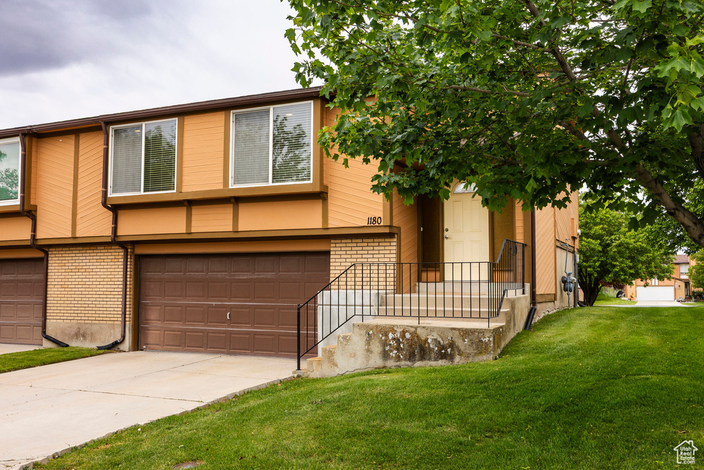 Multi unit property with an attached garage, brick siding, concrete driveway, and a front yard
