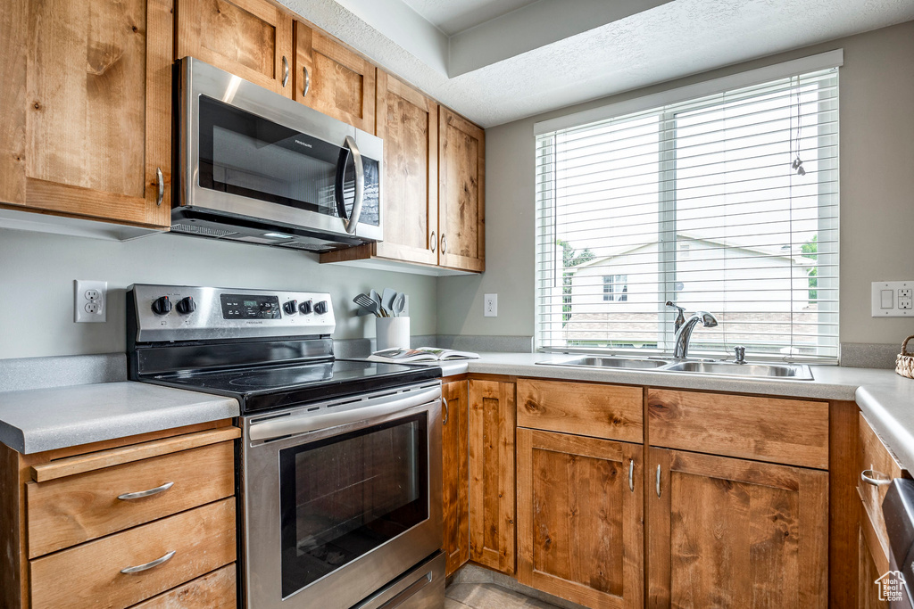 Kitchen with stainless steel appliances, a sink, brown cabinetry, and light countertops