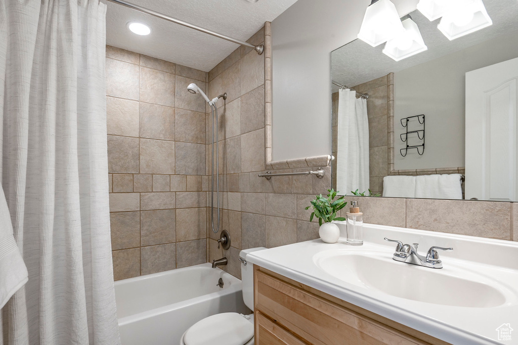 Full bath featuring shower / tub combo with curtain, vanity, tile walls, toilet, and a textured ceiling
